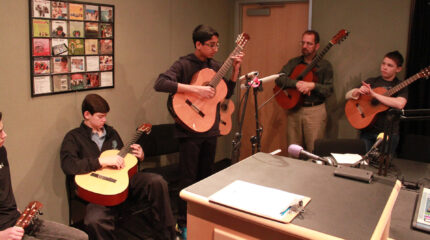 Three youth and an adult holding acoustic guitars in a radio studio