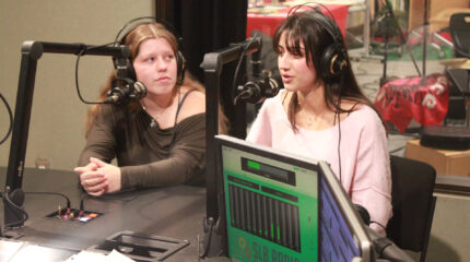 Two teens wearing headphones speaking into microphones in a radio studio