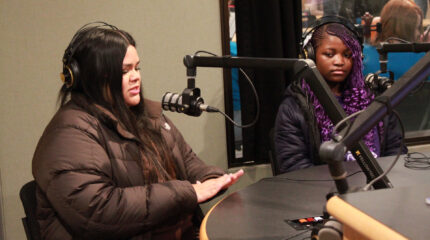 Two teens wearing headphones speaking into microphones in a radio studio