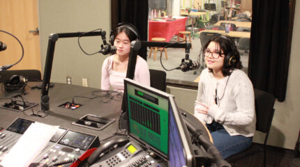 Two teens wearing headphones speaking into microphones in a radio studio
