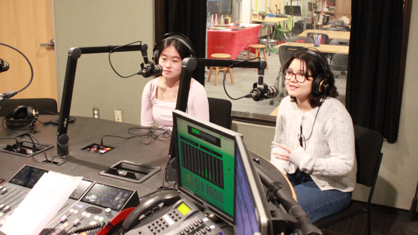 Two teens wearing headphones speaking into microphones in a radio studio