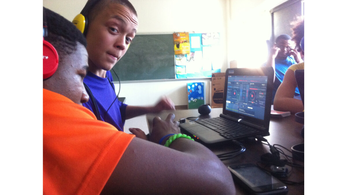 Two youth wearing headphones looking at audio software on a laptop computer in a classroom