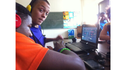 Two youth wearing headphones looking at audio software on a laptop computer in a classroom