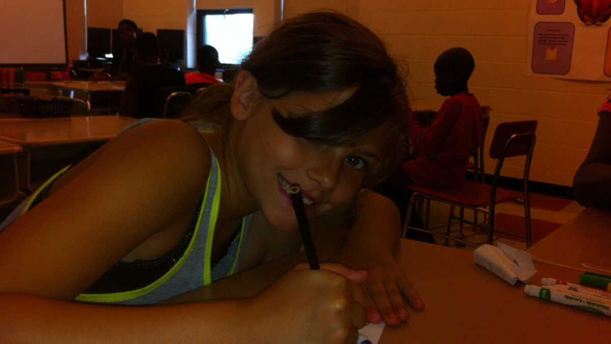 A youth drawing on a piece of paper with a black colored pencil in a classroom