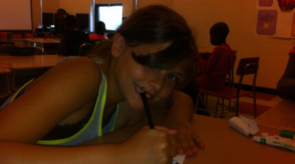 A youth drawing on a piece of paper with a black colored pencil in a classroom