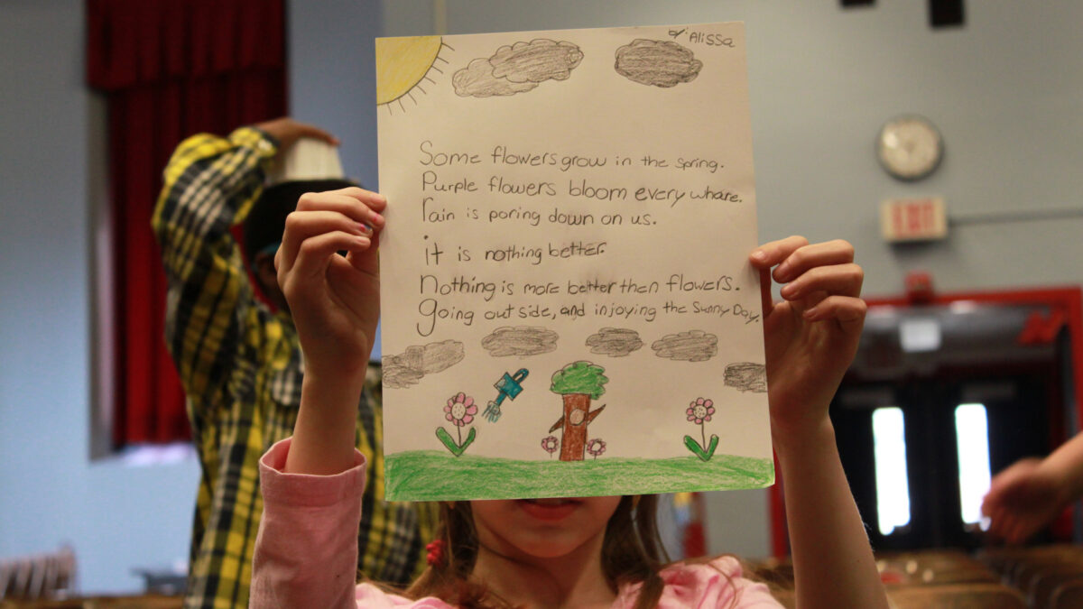 A youth holding up a piece of paper with a poem and drawings of the sun, clouds, flowers, a tree, and a watering can on it