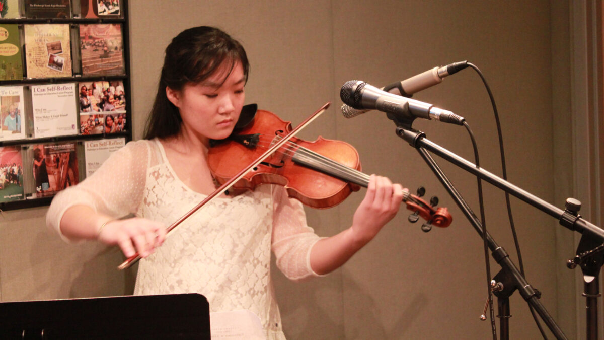 A teen playing violin in front of two microphones in a radio studio