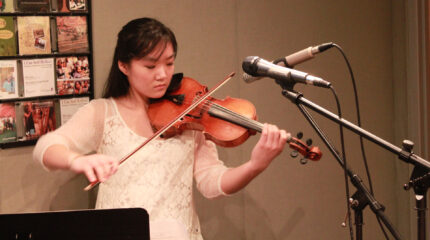 A teen playing violin in front of two microphones in a radio studio