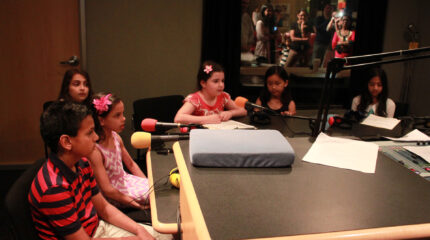 Six youth speaking into microphones in a radio studio
