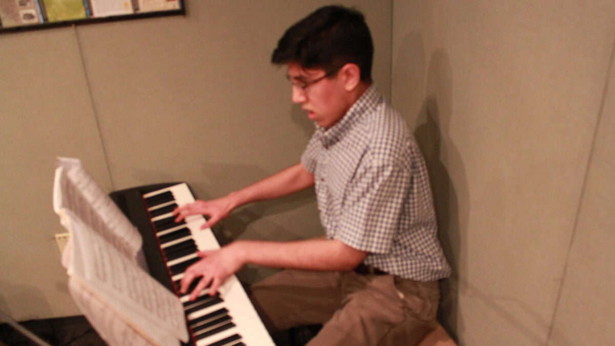 A teen playing a piano keyboard looking at sheet music in a radio studio.