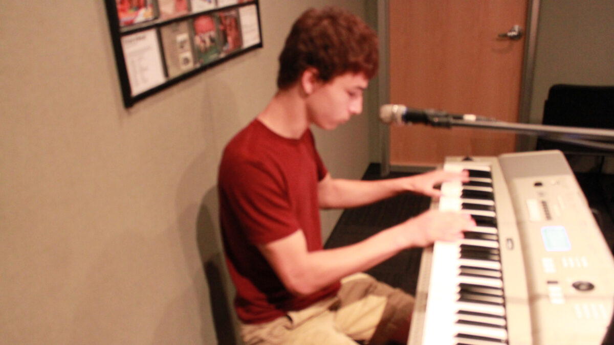 A teen playing a piano keyboard sitting behind a microphone in a radio studio
