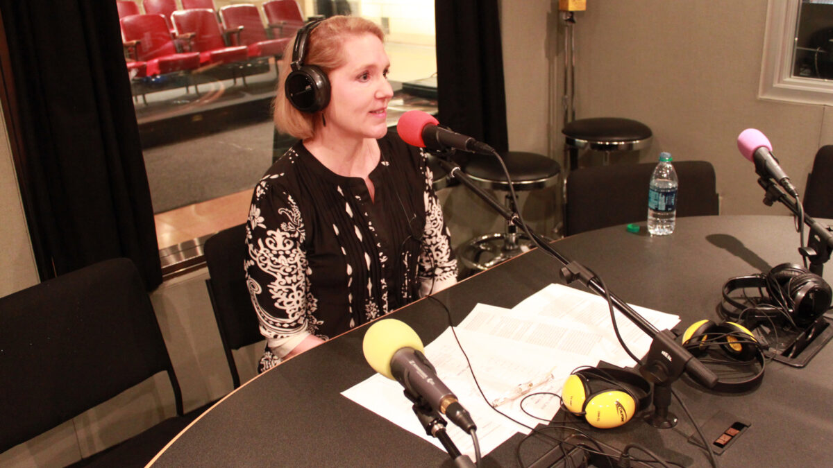 An adult wearing headphones speaking into a microphone in a radio studio