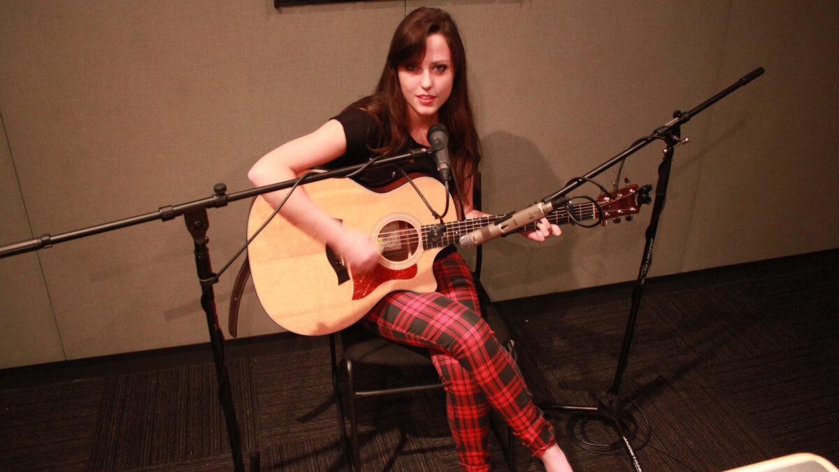 A teen playing an acoustic guitar and singing into a microphone in a radio studio