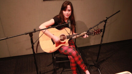A teen playing an acoustic guitar and singing into a microphone in a radio studio
