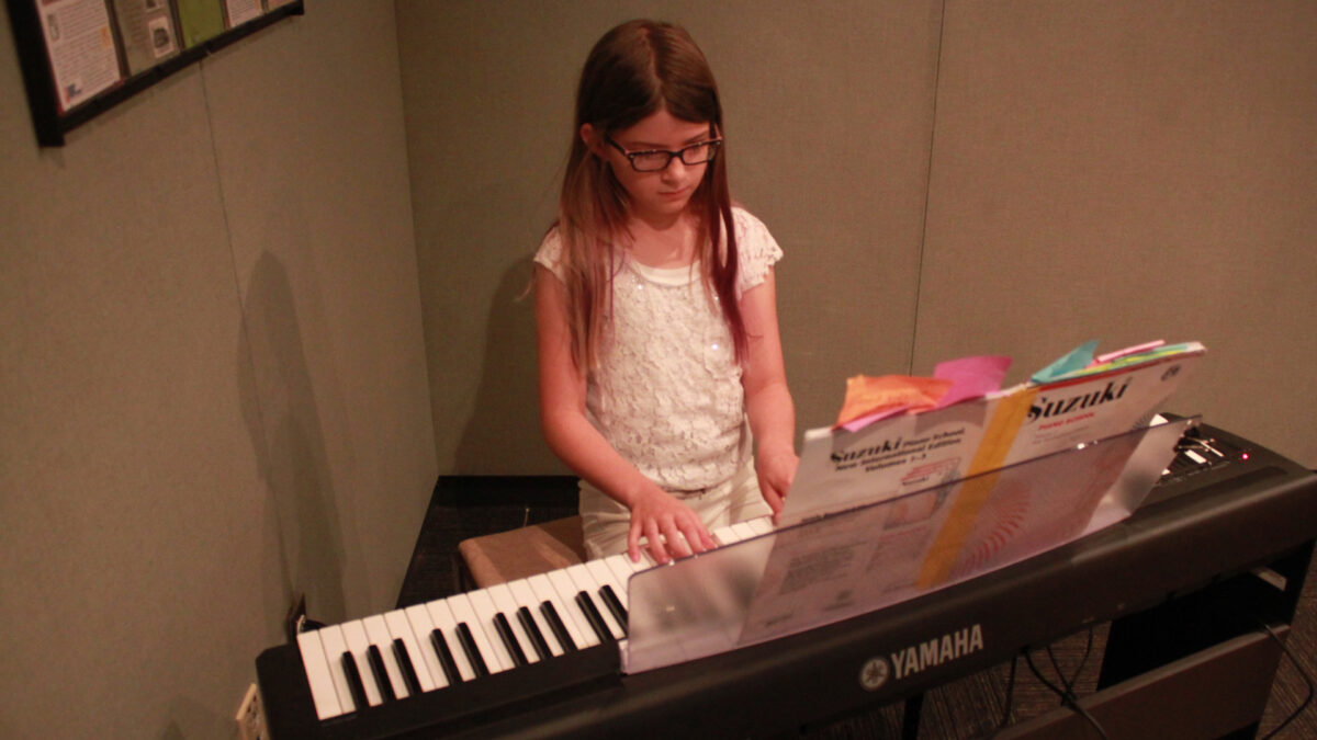A youth playing a piano keyboard looking at sheet music in a radio studio