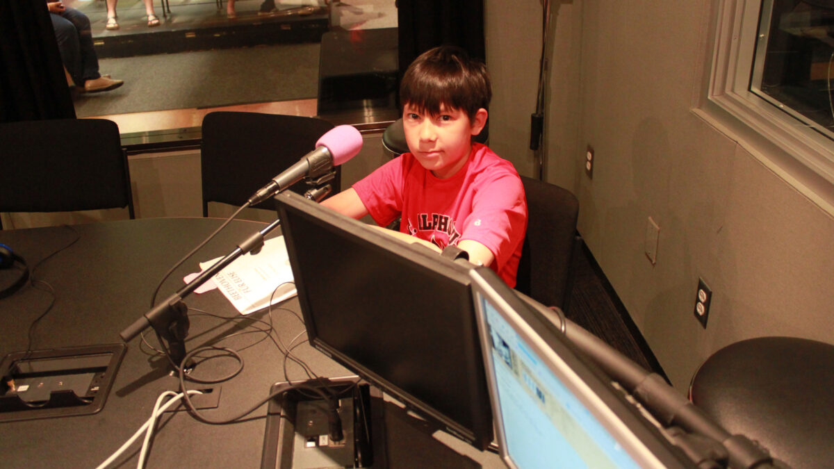 A youth sitting behind a microphone in a radio studio