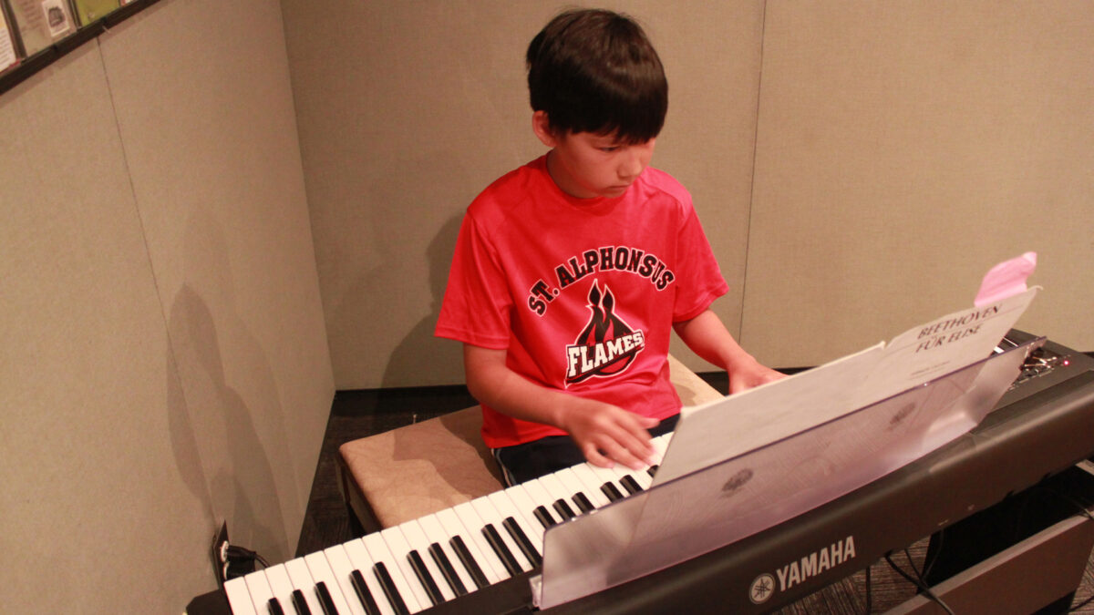 A youth playing a piano keyboard looking at sheet music in a radio studio