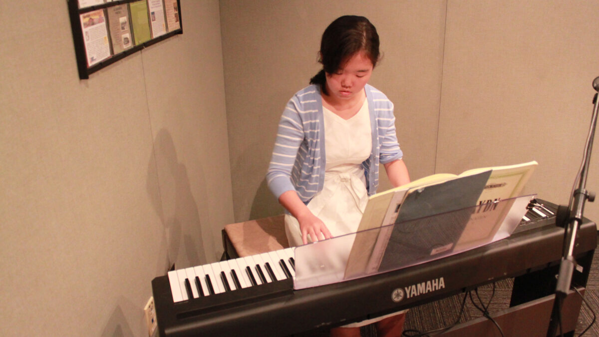A teen playing a piano keyboard looking at sheet music in a radio studio