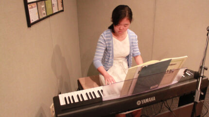 A teen playing a piano keyboard looking at sheet music in a radio studio