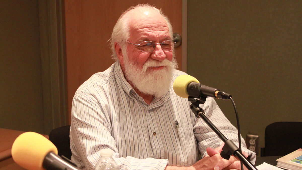 An adult smiling while sitting behind a microphone in a radio studio