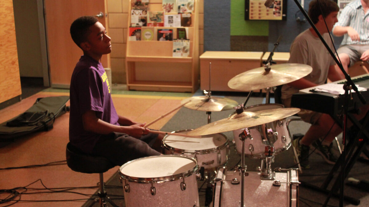 A youth playing a drum set and a teen sitting behind a piano keyboard