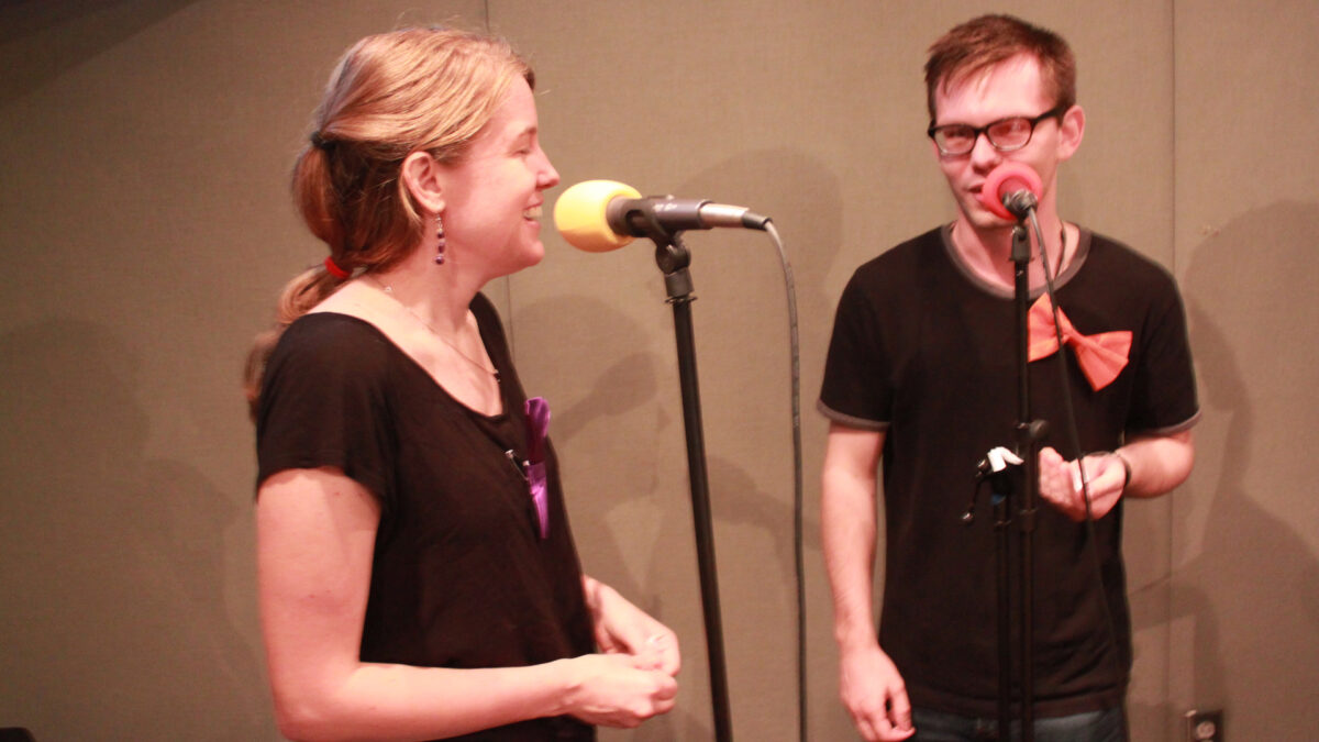 Two adults smiling while speaking into microphones in a radio studio