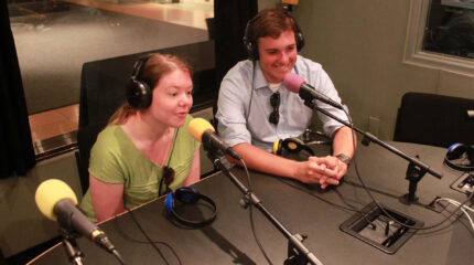 Two teens wearing headphones speaking into microphones in a radio studio