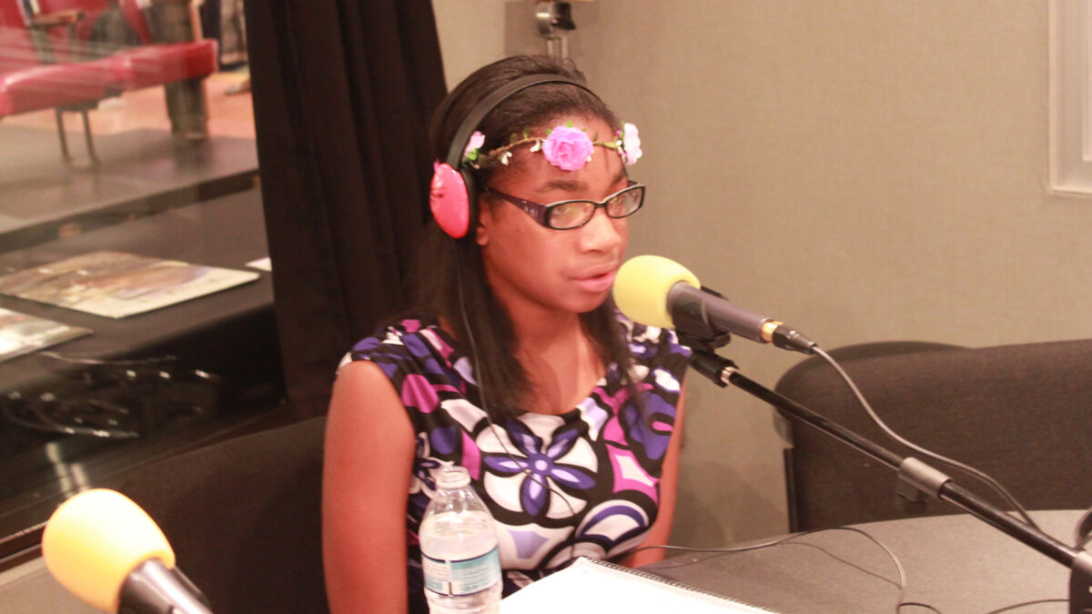 A teen wearing headphones speaking into a microphone in a radio studio