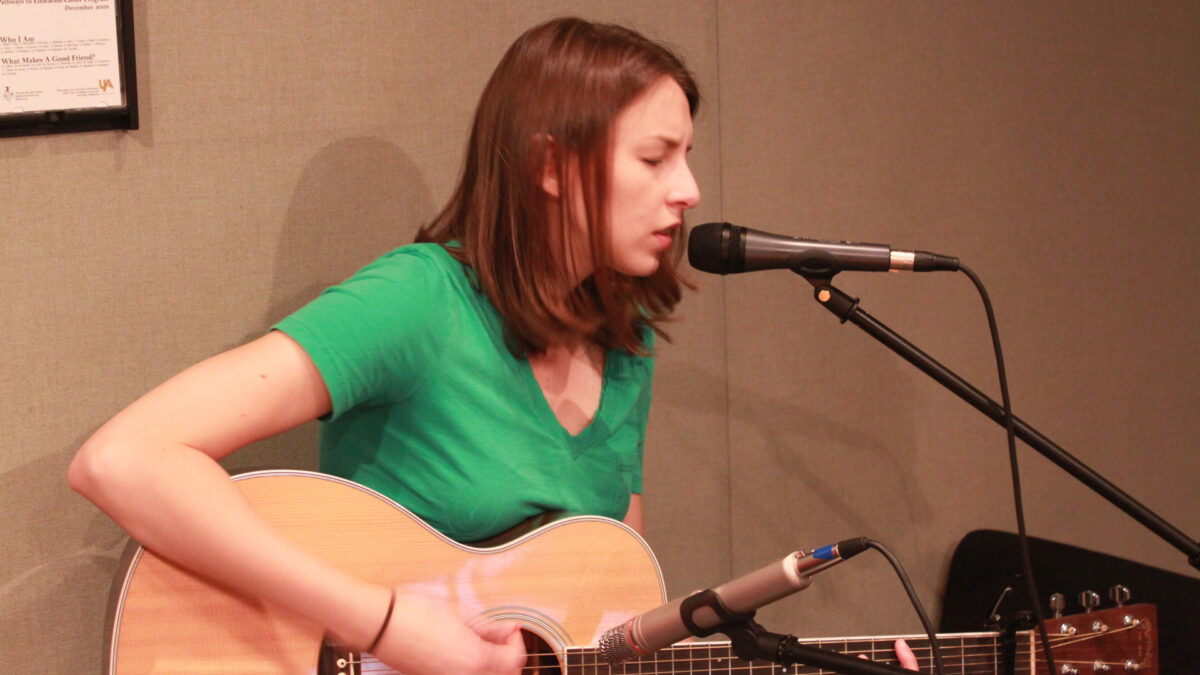 An adult playing an acoustic guitar and singing into a microphone in a radio studio