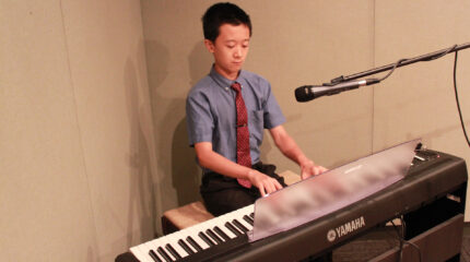 A youth playing a piano keyboard sitting behind a microphone in a radio studio