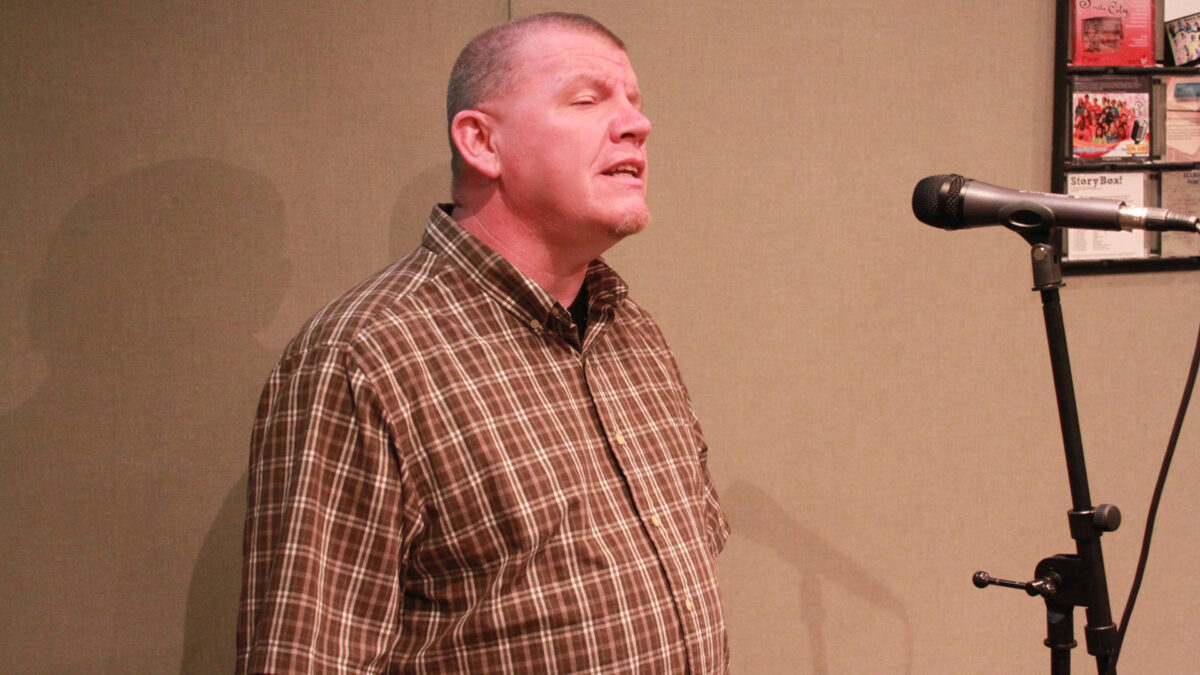 An adult singing into a microphone in a radio studio