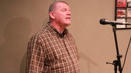 An adult singing into a microphone in a radio studio