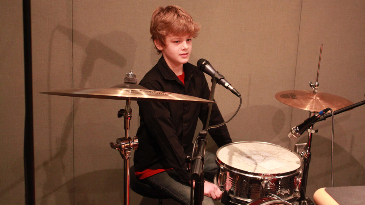 A youth sitting behind a drum set in a radio studio
