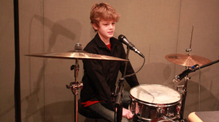 A youth sitting behind a drum set in a radio studio