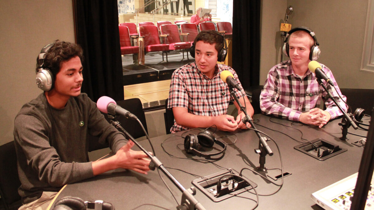 Three teens wearing headphones speaking into microphones in a radio studio