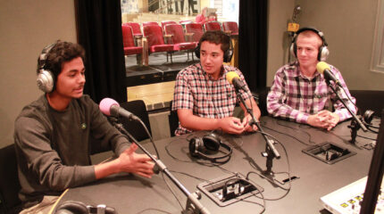 Three teens wearing headphones speaking into microphones in a radio studio