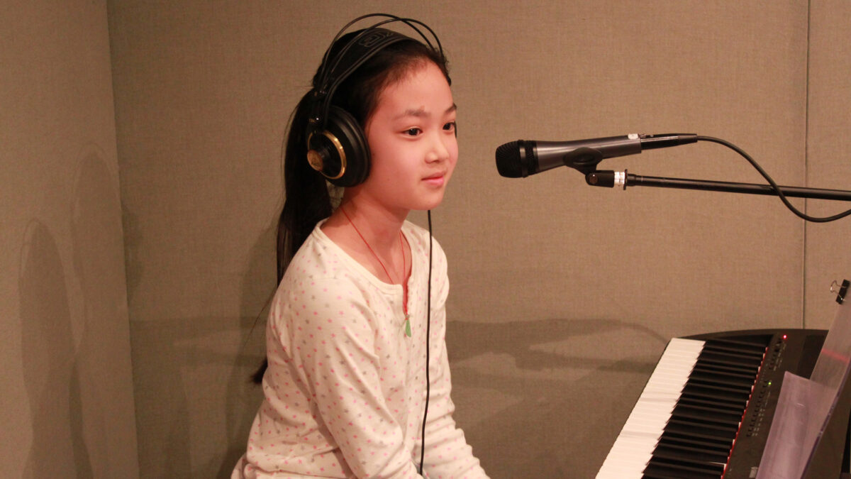 A youth wearing headphones sitting behind a piano keyboard and a microphone in a radio studio