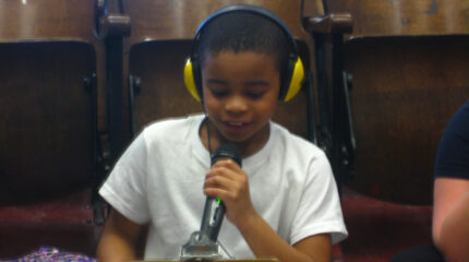 A youth wearing headphones holding and speaking into a microphone