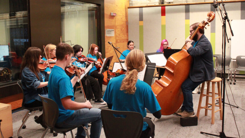 Eight individuals playing string instruments around an adult playing an upright bass in an orchestra