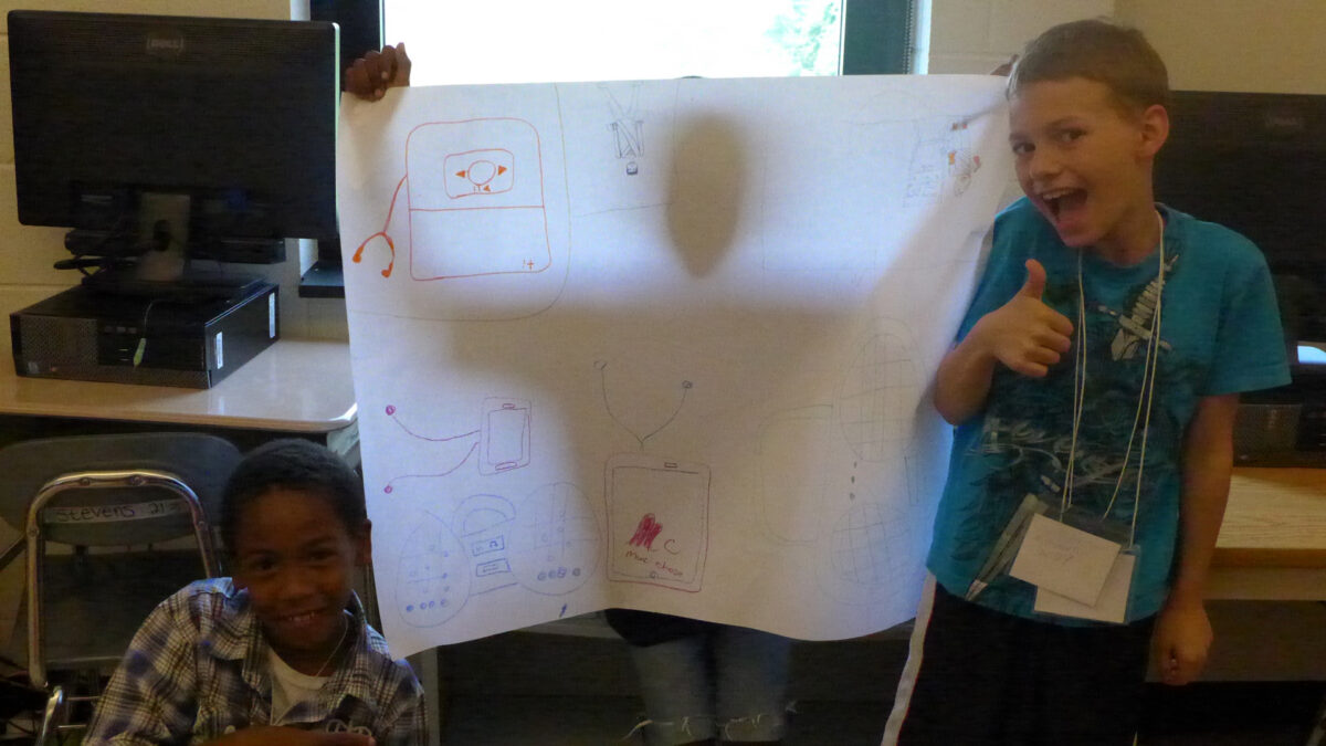 Two youth posing next to a youth holding a large piece of poster paper in front of them casting them in shadow in a classroom