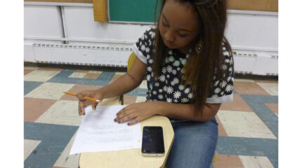 A youth holding a pencil and looking down at a piece of paper on a classroom desk
