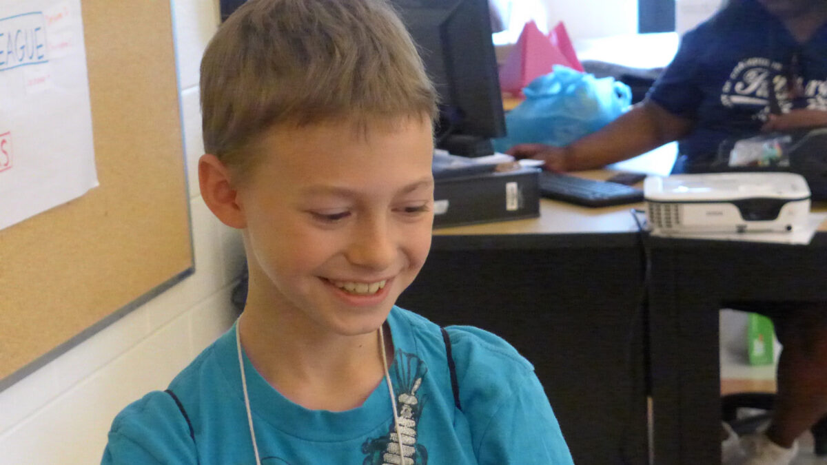 A youth smiling while looking down to the right in a classroom