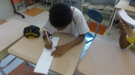 A youth writing on a notepad on a classroom desk