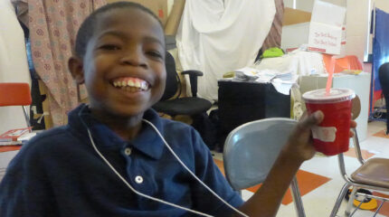 A youth smiling while holding a red plastic cup in a classroom