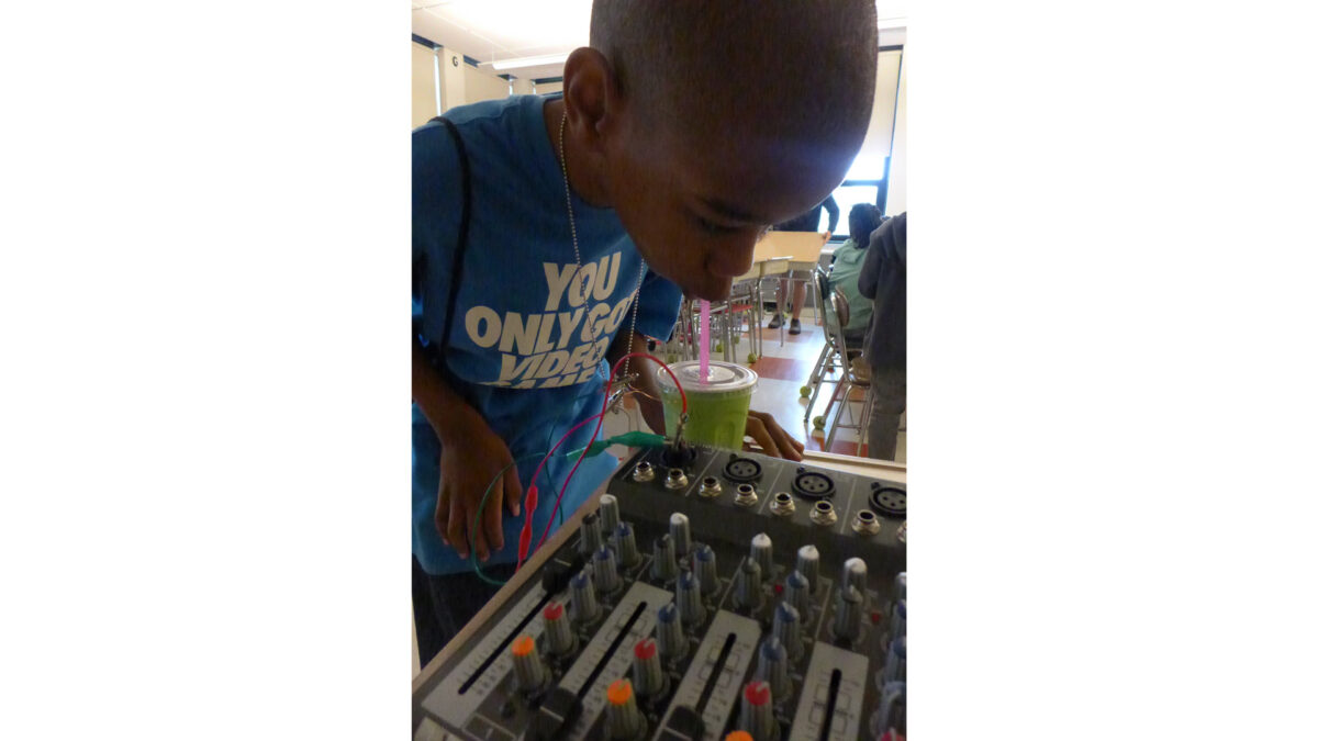 A youth drinking from a green cup as they look over a mixer in a classroom