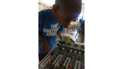 A youth drinking from a green cup as they look over a mixer in a classroom
