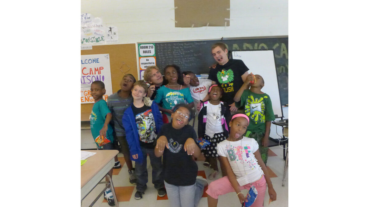 Ten youth and an adult making silly faces and poses at the camera in a classroom