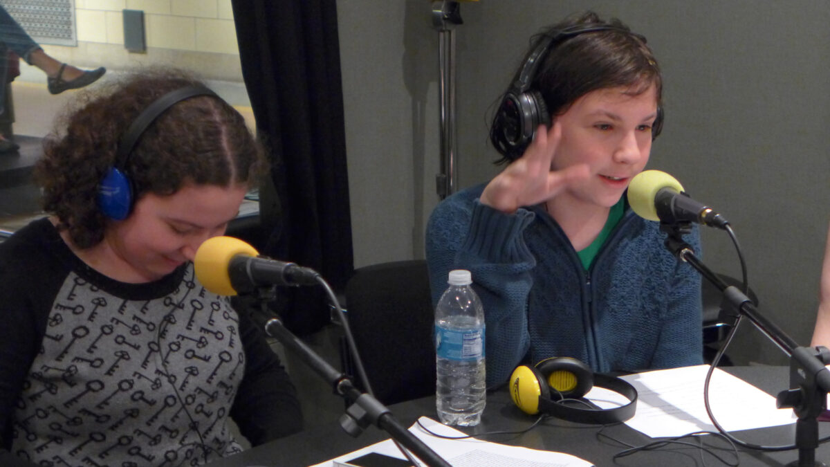 Two youth wearing headphones speaking into microphones in a radio studio