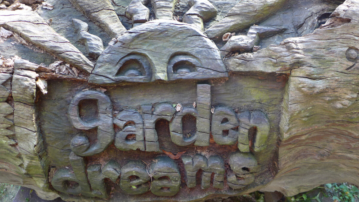 A sculpture of a sun and the text "garden dreams", both carved out of the same bark on a log