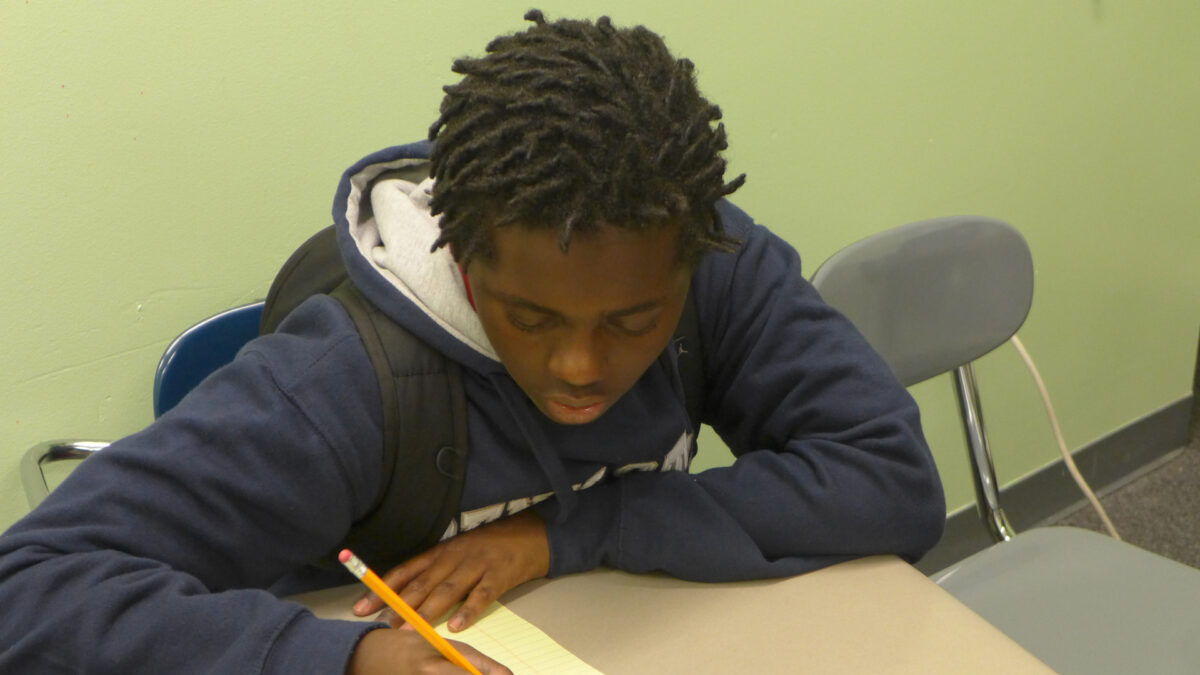 A youth writing on a piece of paper on a classroom desk